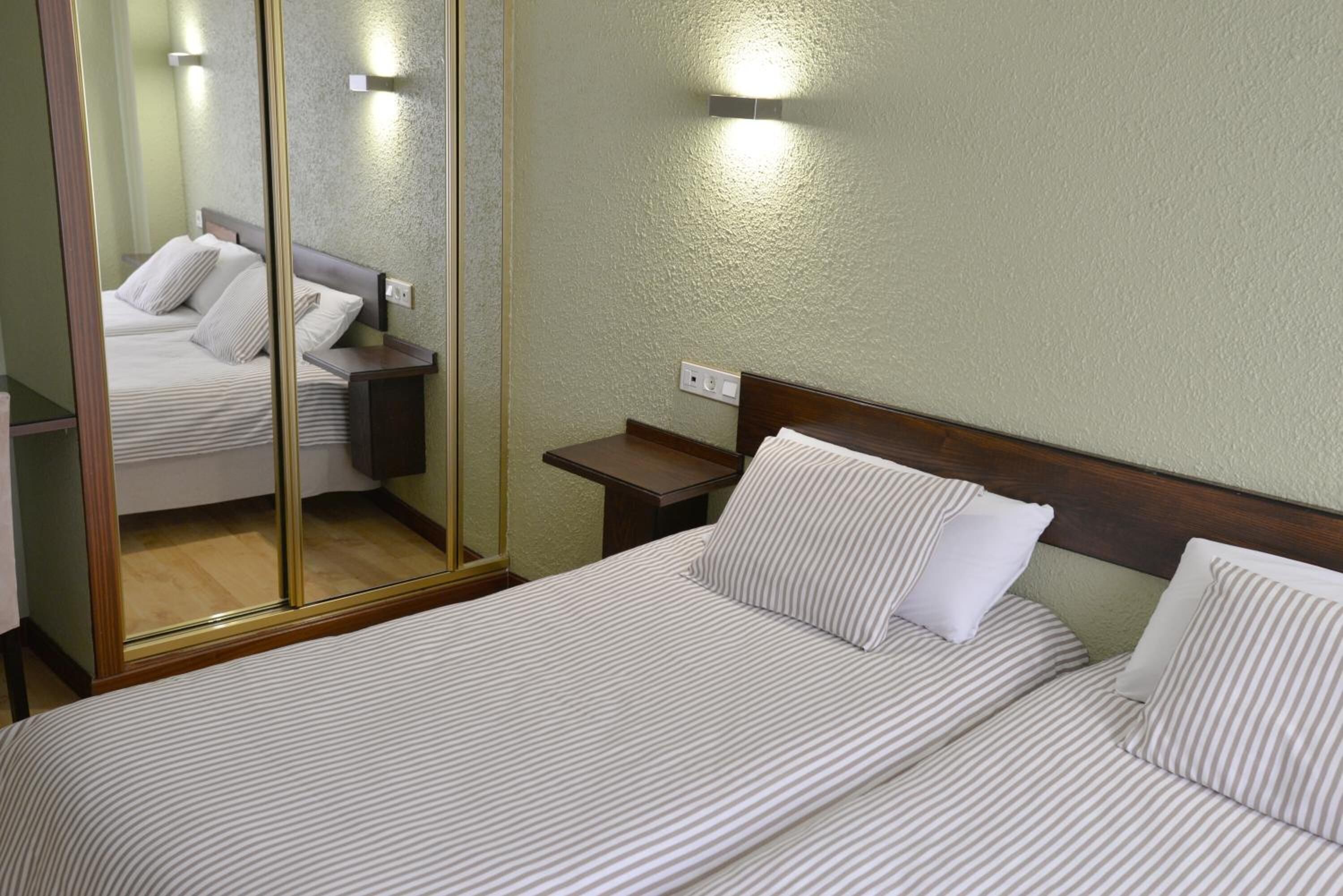 A hotel room with a large mirror, a wooden headboard, a bedside table, and a bed with striped bedding.