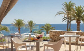 An outdoor dining area with tables and chairs, overlooking the sea.