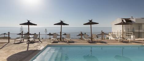 Una piscina al aire libre, sombrillas, sillones reclinables de piscina