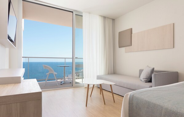 A modern hotel room with a balcony, a sofa, a small table, and a bed.