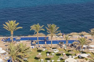 Un área de piscina con varias piscinas, palmeras y tumbonas.