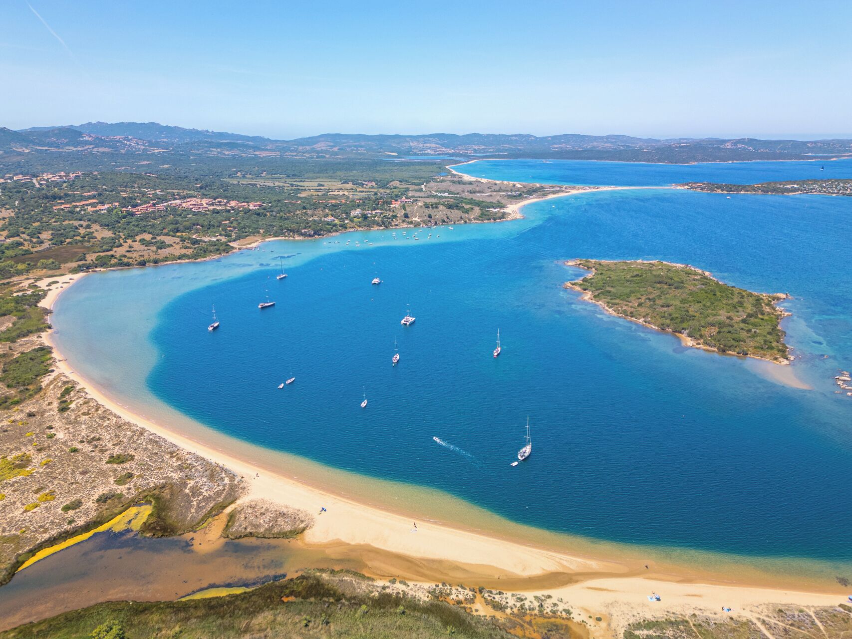 Vista aérea de una zona costera con aguas azules cristalinas, playas de arena y algunas embarcaciones.