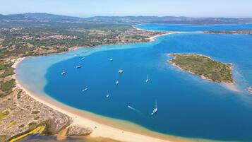 Vista aérea de una zona costera con aguas azules cristalinas, playas de arena y algunas embarcaciones.
