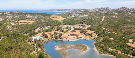 An aerial view of a coastal resort with multiple buildings, a central lagoon, and surrounding greenery.