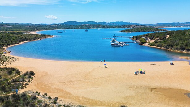 Una spiaggia costiera con acque blu cristalline, imbarcazioni ormeggiate e una battigia sabbiosa.
