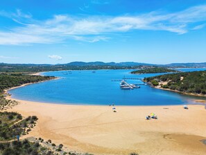 Una playa costera con aguas azules cristalinas, barcos amarrados y una orilla arenosa.