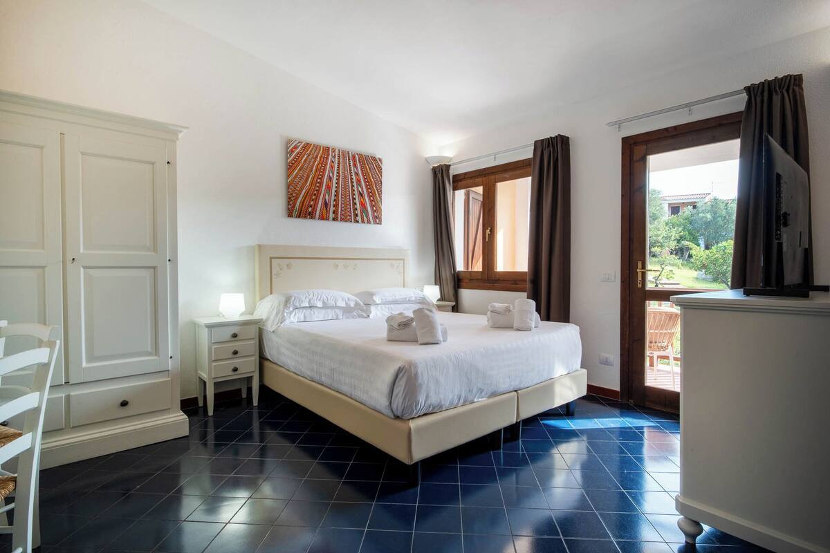 A bedroom with a bed, a nightstand, a wardrobe, and a window with curtains.