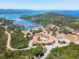Vista aérea de un complejo turístico en la costa con varios edificios, un camino sinuoso y una gran extensión de agua.