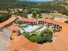 Un resort con piscina central, varias canchas de tenis y un paisaje circundante con árboles y colinas.