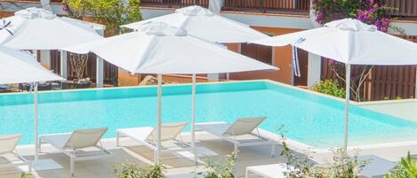 Ett poolområde med vita parasoller och solstolar, omgivet av en byggnad med balkonger och växter.