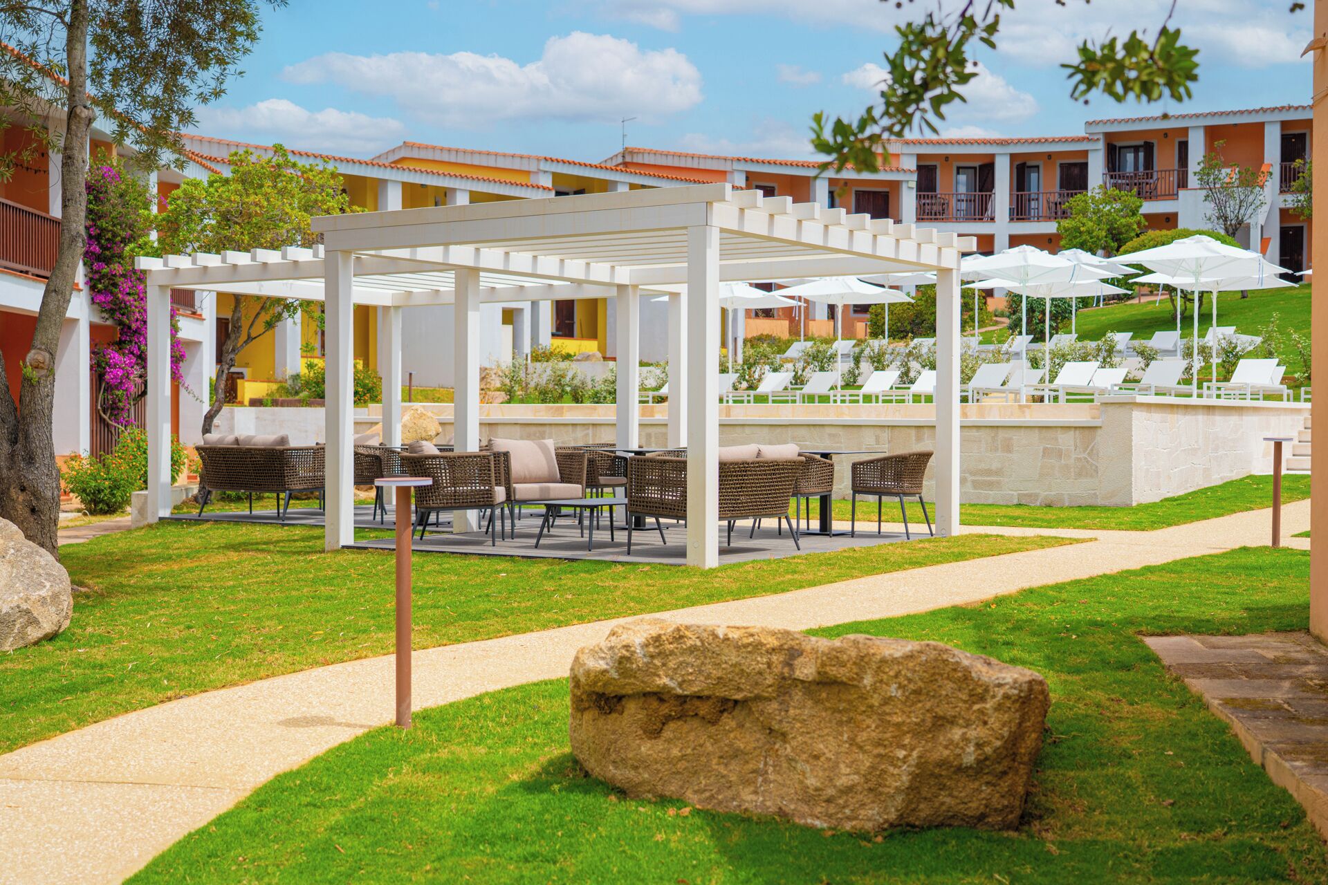 A covered outdoor seating area with tables and chairs, a stone pathway, and a large rock in the foreground.