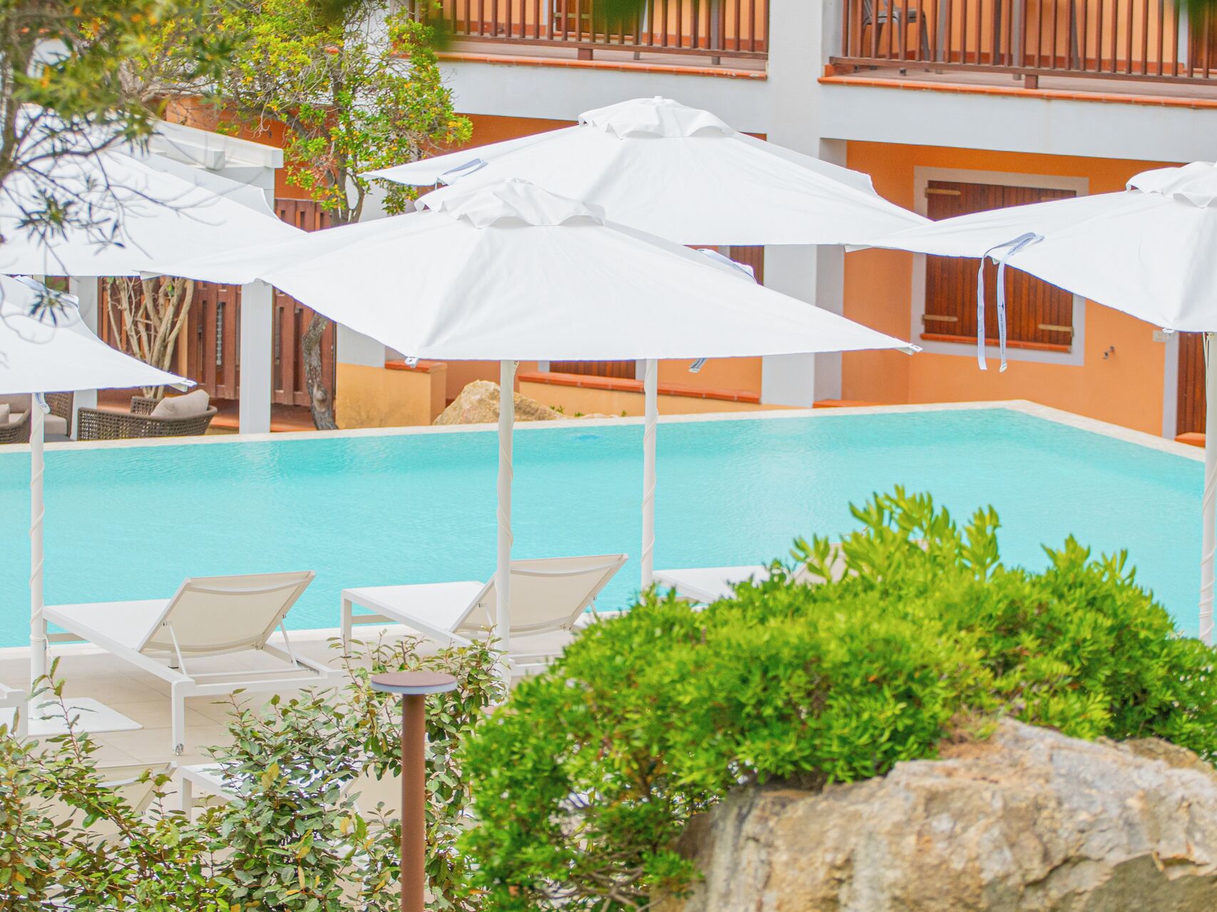 Une zone de piscine avec des parasols blancs, des chaises longues et un bâtiment doté de balcons en arrière-plan.