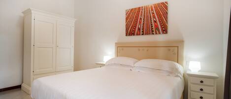 A bedroom with a large bed, a nightstand, a wardrobe, and a wall-mounted artwork.