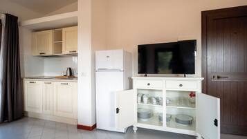 Cocina compacta con armarios blancos, refrigerador empotrado, microondas y televisor sobre un mueble.