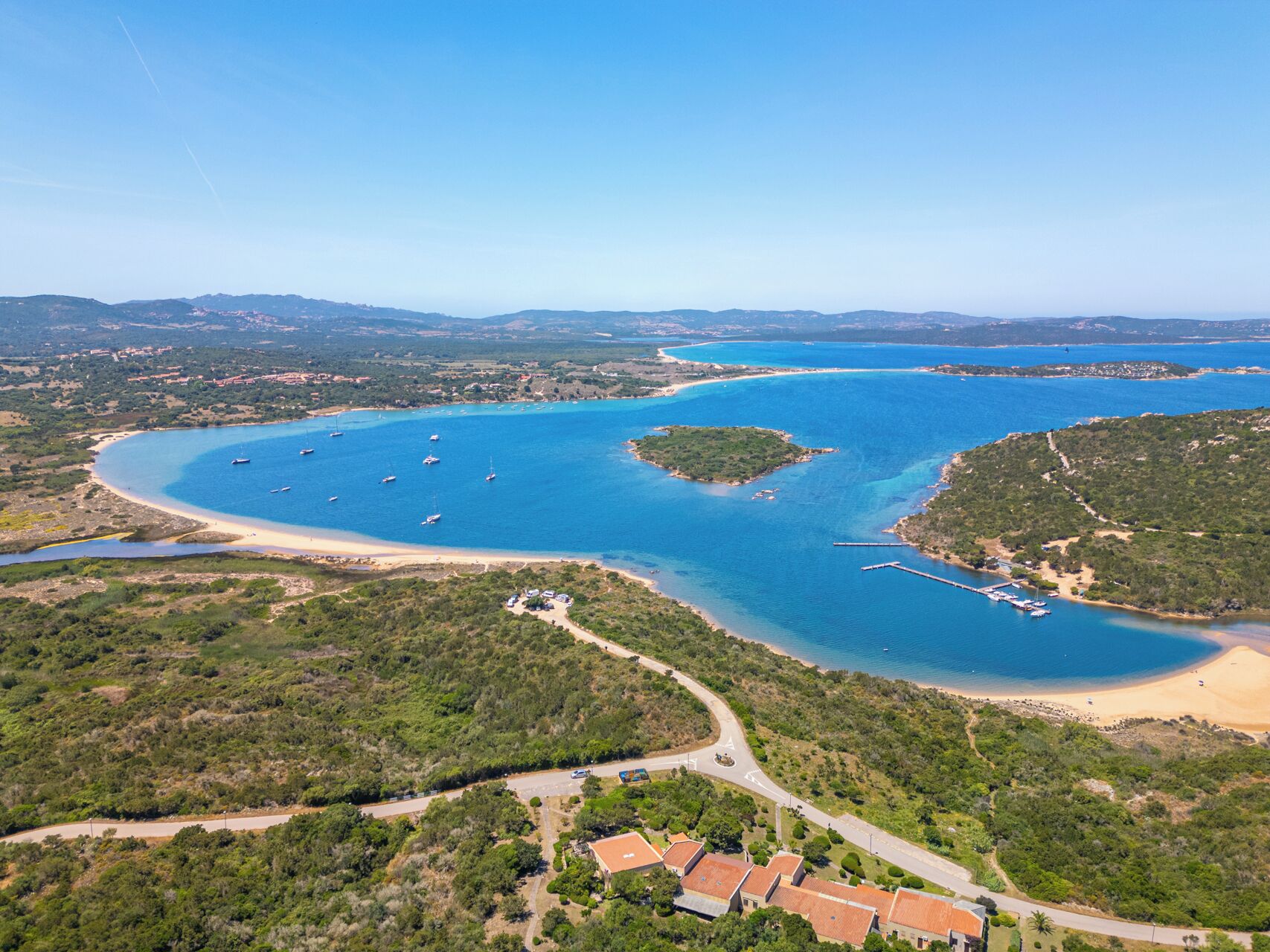 Vista aérea de una zona costera con un puerto deportivo, playas de arena y vegetación circundante.