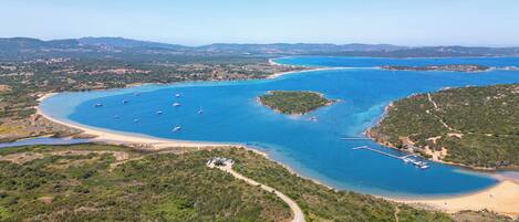 An aerial view of a coastal area with a marina, sandy beaches, and surrounding greenery.