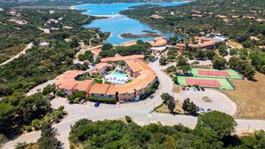 Vista aerea di un resort costiero con piscina, campi da tennis e una strada che conduce agli edifici.