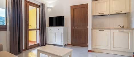 A room with a sofa, a table, a TV, a sliding door, and a kitchen area with cabinets.