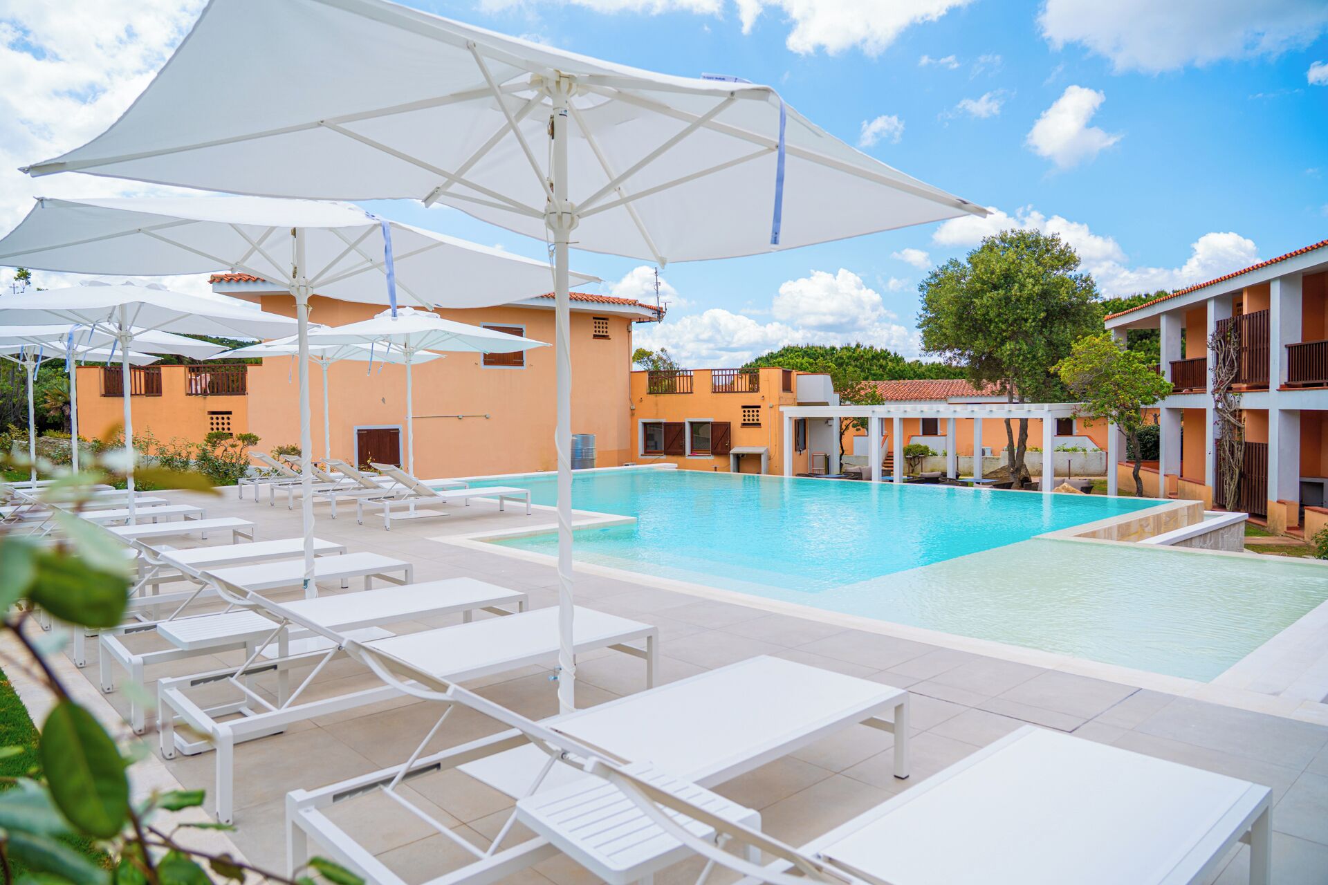 A pool area with sun loungers and umbrellas, surrounded by buildings with balconies.