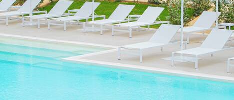 A swimming pool with white lounge chairs and umbrellas.