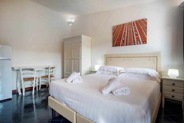 Habitación de hotel con cama, escritorio, silla, armario y un cuadro en la pared.