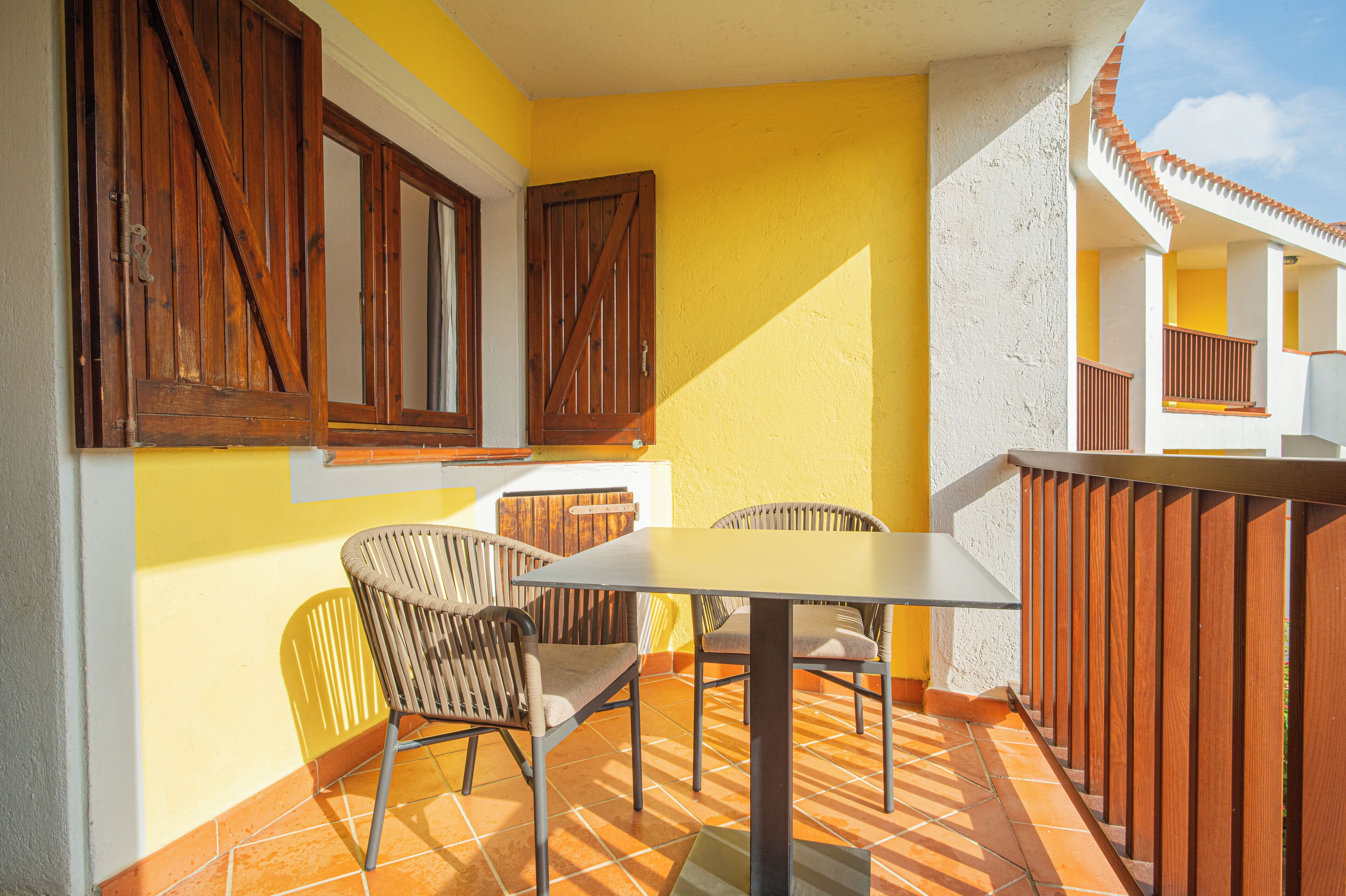 A patio with a table and chairs, wooden shutters, and a tiled floor.