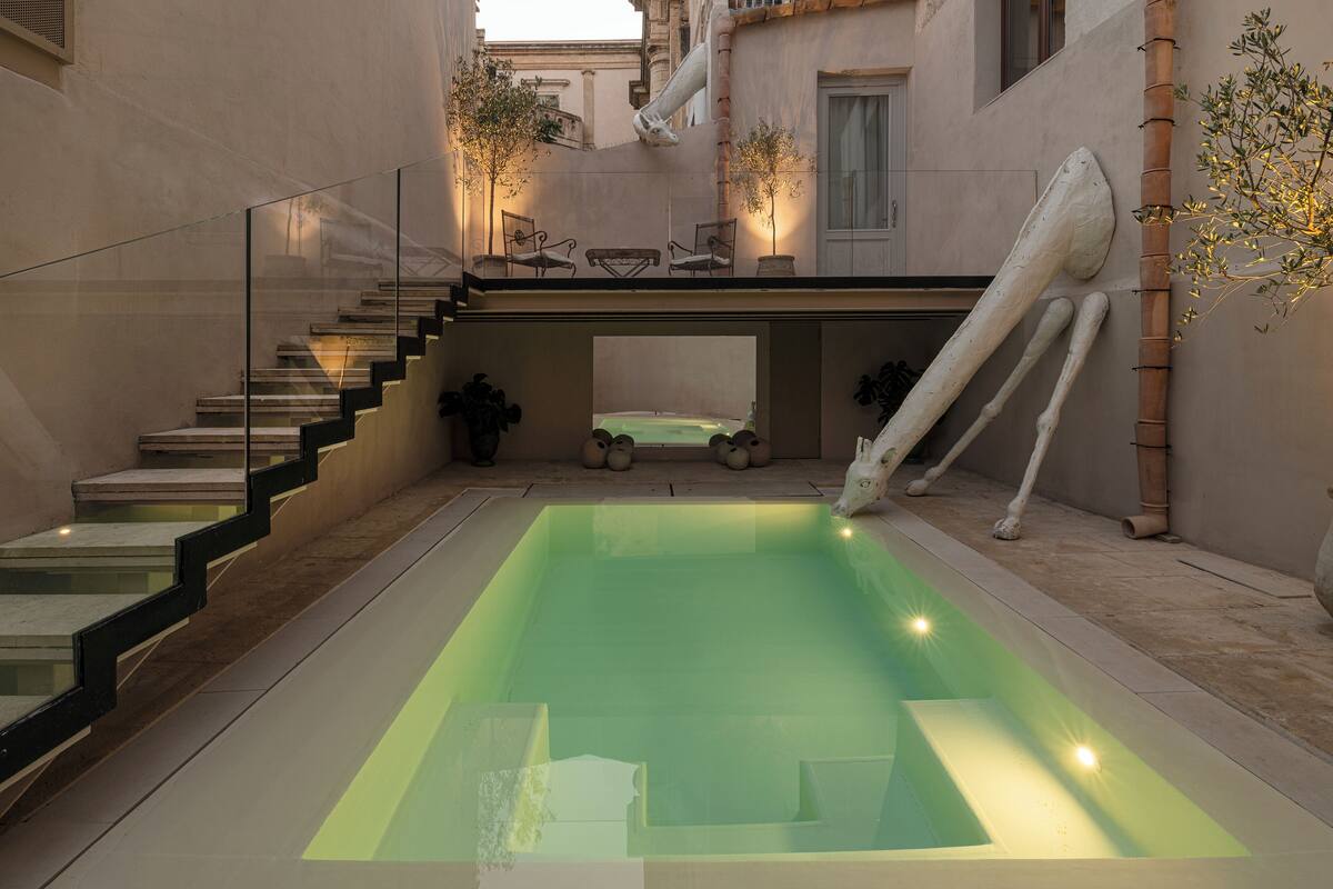 A modern pool area with a glass-enclosed staircase, a hot tub, and a unique sculpture.