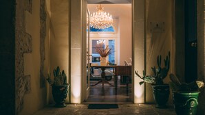 Um corredor com um candelabro, cactos em vasos e uma área de jantar ao fundo.