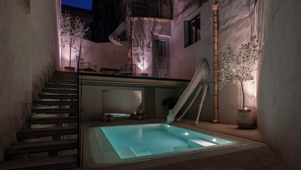 Uma área de piscina moderna ao ar livre, com um revestimento de vidro, uma escadaria e um pequeno espaço para sentar.