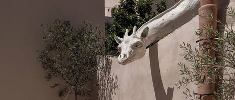 Un patio con sillas y una mesa de metal, una palmera alta y una escultura de jirafa.