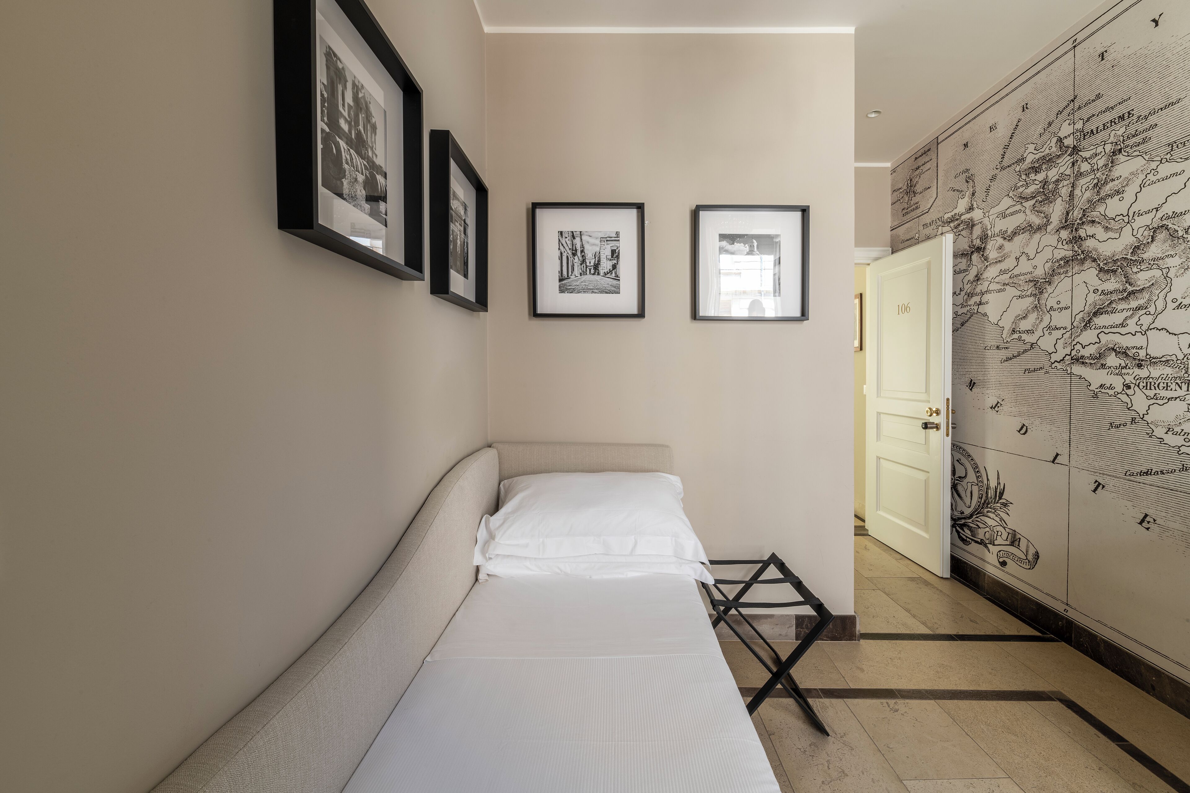 Un pasillo estrecho con una cama, cuadros en la pared y un mapa.