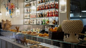 Uma área de bar com prateleiras cheias de garrafas de bebidas, uma vitrine de vidro com petiscos e objetos decorativos.