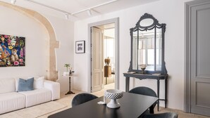 Uma sala de estar moderna com um sofá branco, uma mesa de jantar preta e um espelho decorativo.