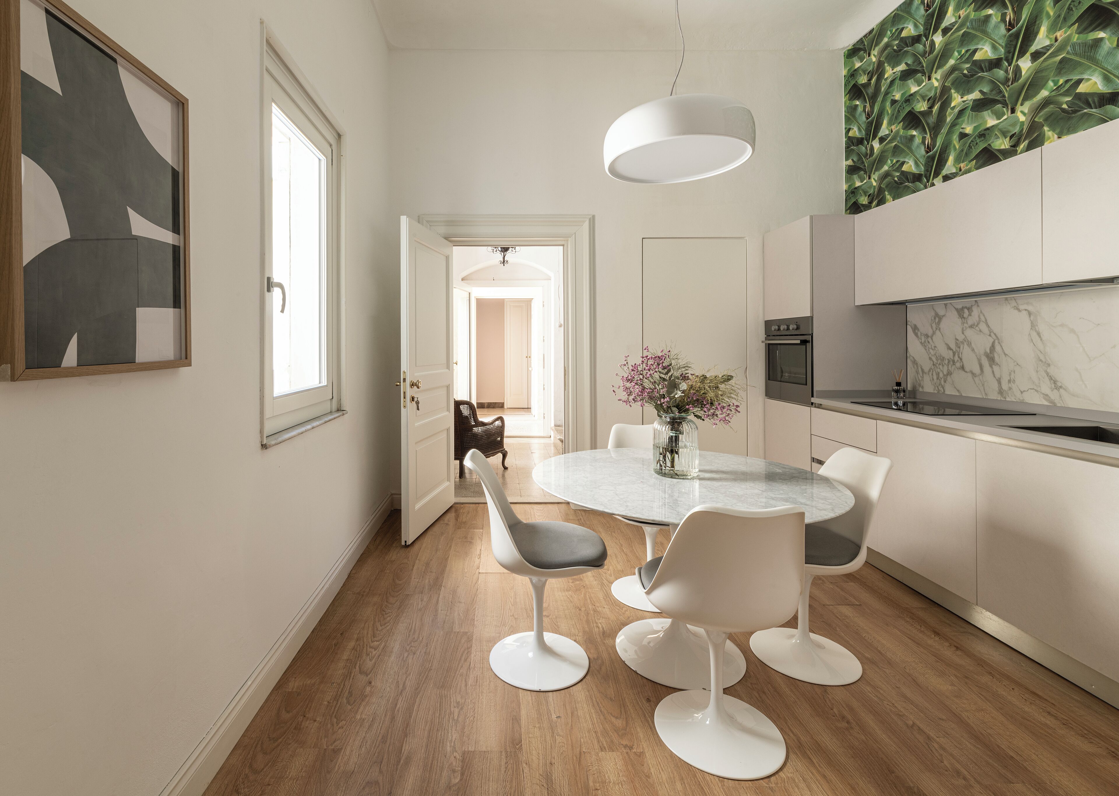 A modern kitchen with a marble backsplash, a built-in oven, and a dining area with a round table and white chairs.