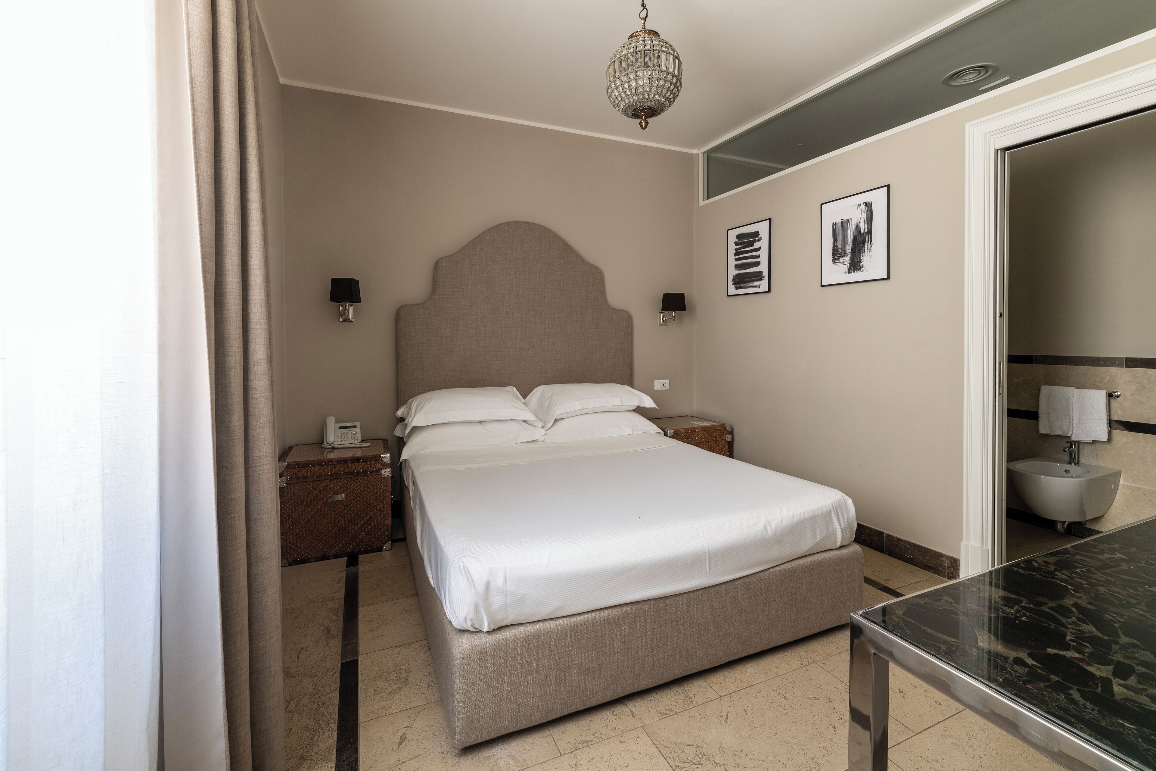 Habitación de hotel con una cama grande, mesitas de noche, lámpara de noche, candelabro y baño con bañera.