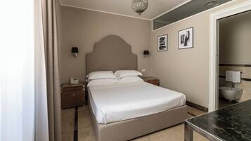 Habitación de hotel con una cama grande, mesitas de noche, lámpara de noche, candelabro y baño con bañera.