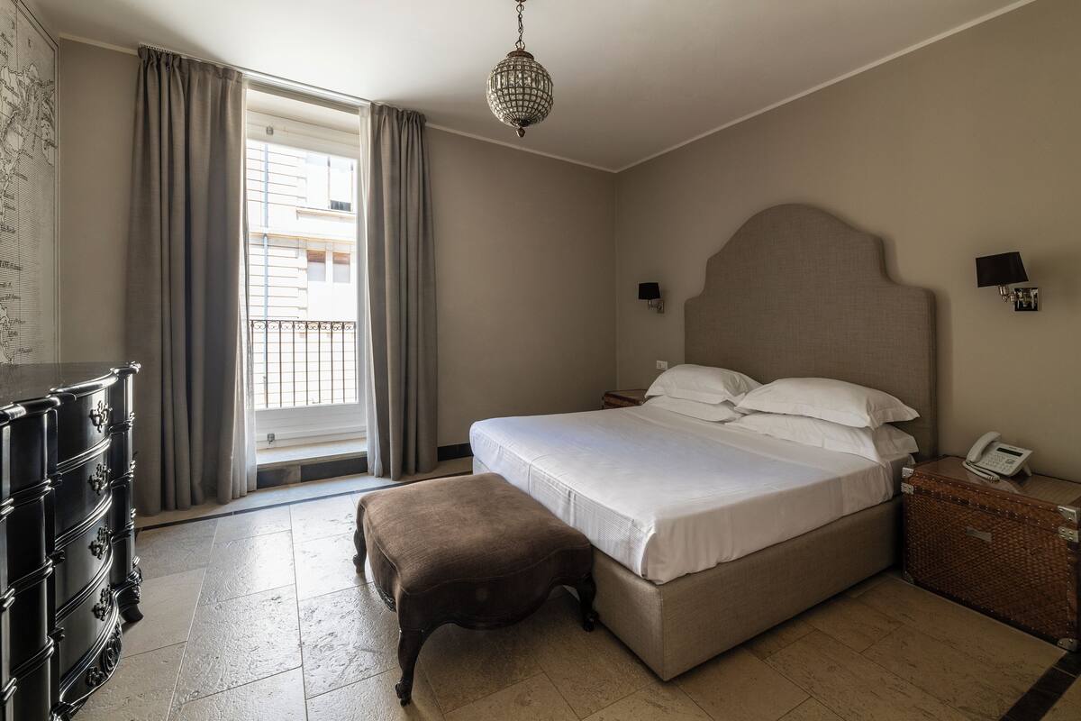 A neatly arranged bedroom with a large bed, a dresser, a bench, and a suitcase.