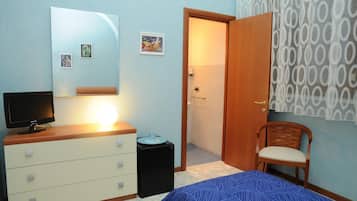 Une chambre à coucher comprenant un lit, une commode, un téléviseur et une porte donnant sur une salle de bain.