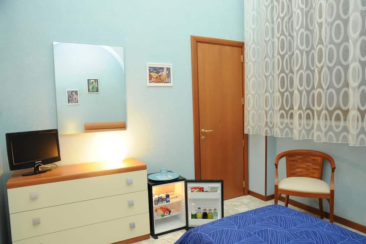 Une chambre à coucher avec un lit, une commode avec un miroir, un petit réfrigérateur, une chaise et une porte.