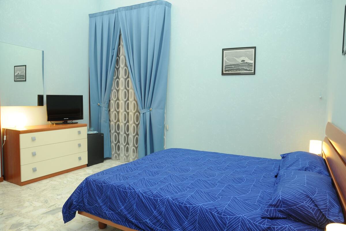 Une chambre à coucher avec un lit, une commode, un téléviseur et un rideau à motifs.