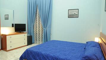 A bedroom with a bed, a dresser, a television, and a patterned curtain.