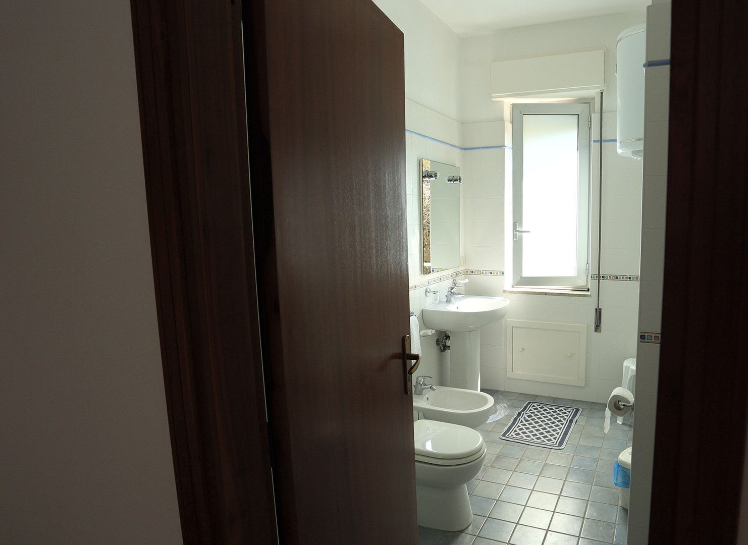 Een badkamer met toilet, bidet, wastafel en spiegel.