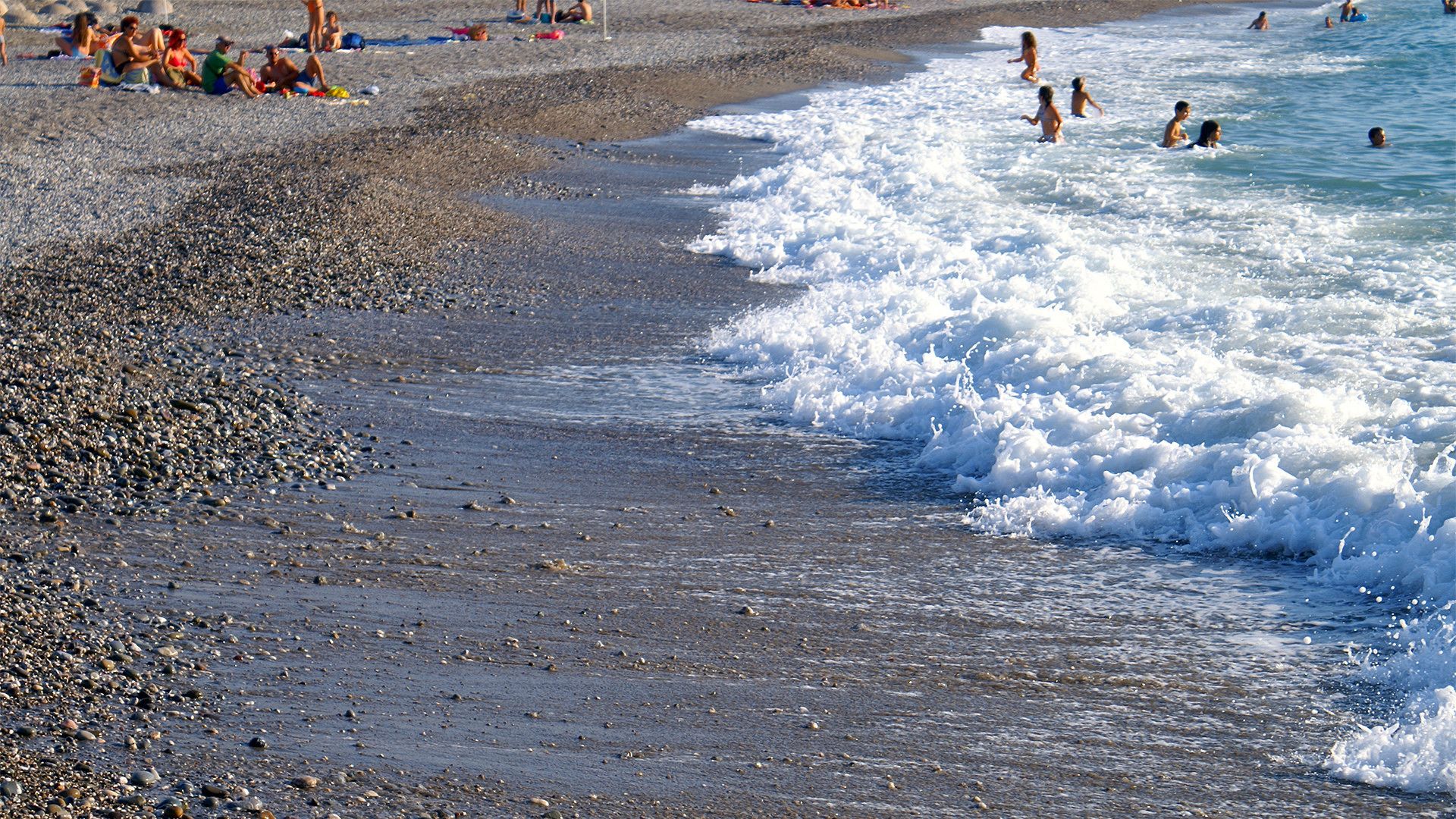 A pebbled beach with people sunbathing and swimming.