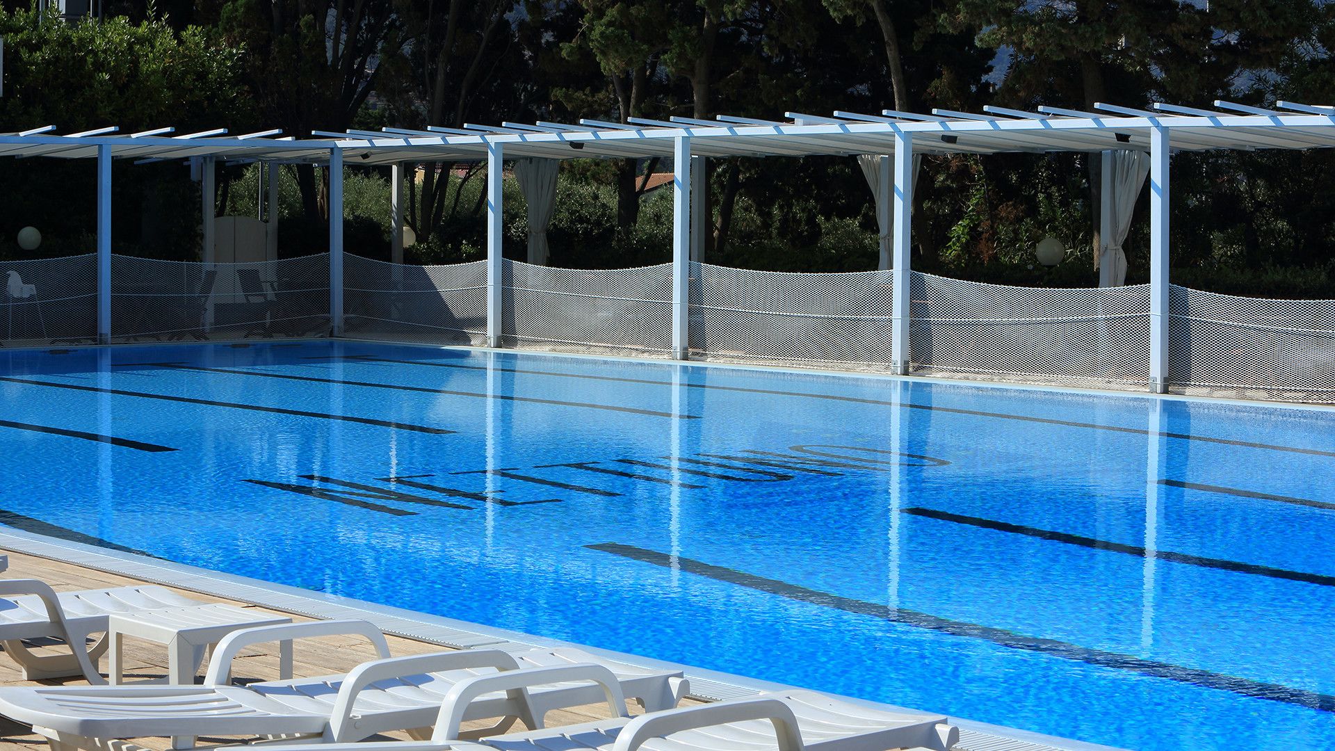 A swimming pool with clear blue water, surrounded by a white fence and covered by a white canopy.