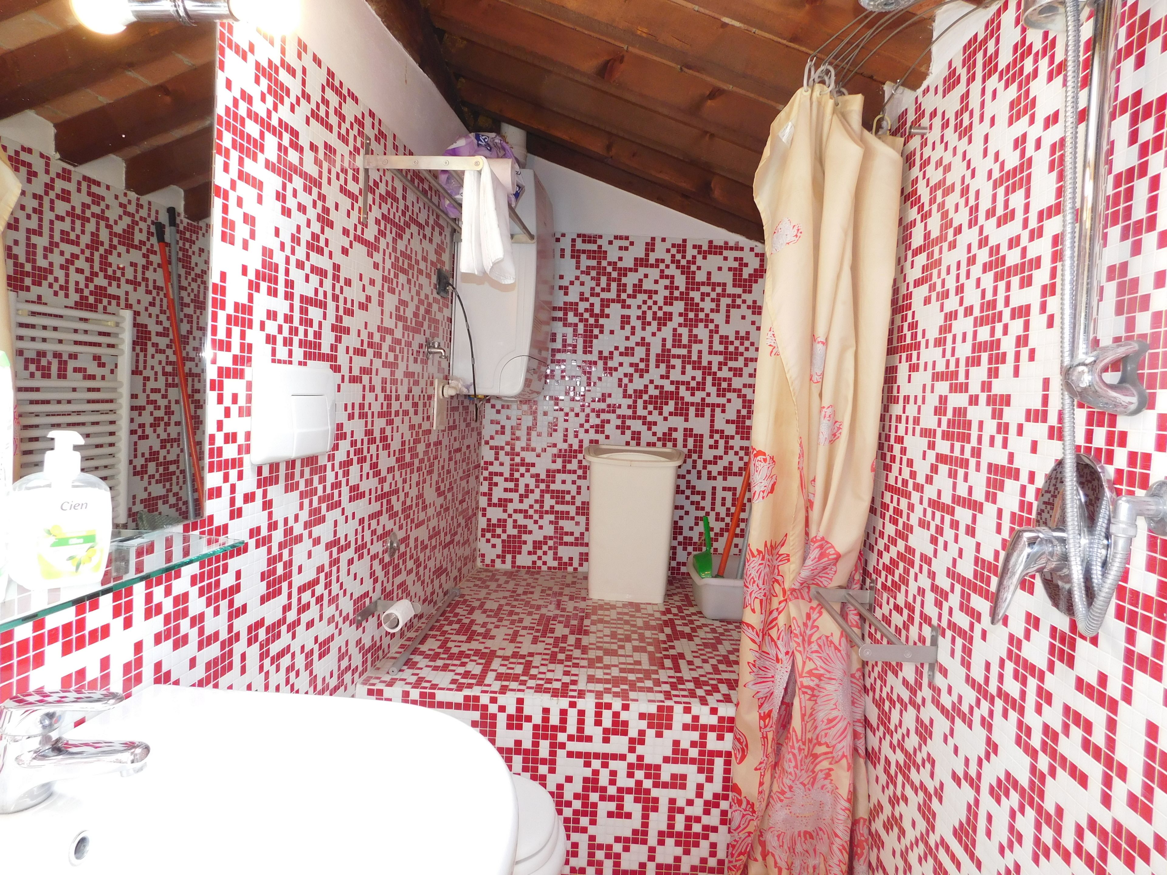 A bathroom with red and white mosaic tile walls, a shower with a beige curtain, and a glass sink with a white faucet.