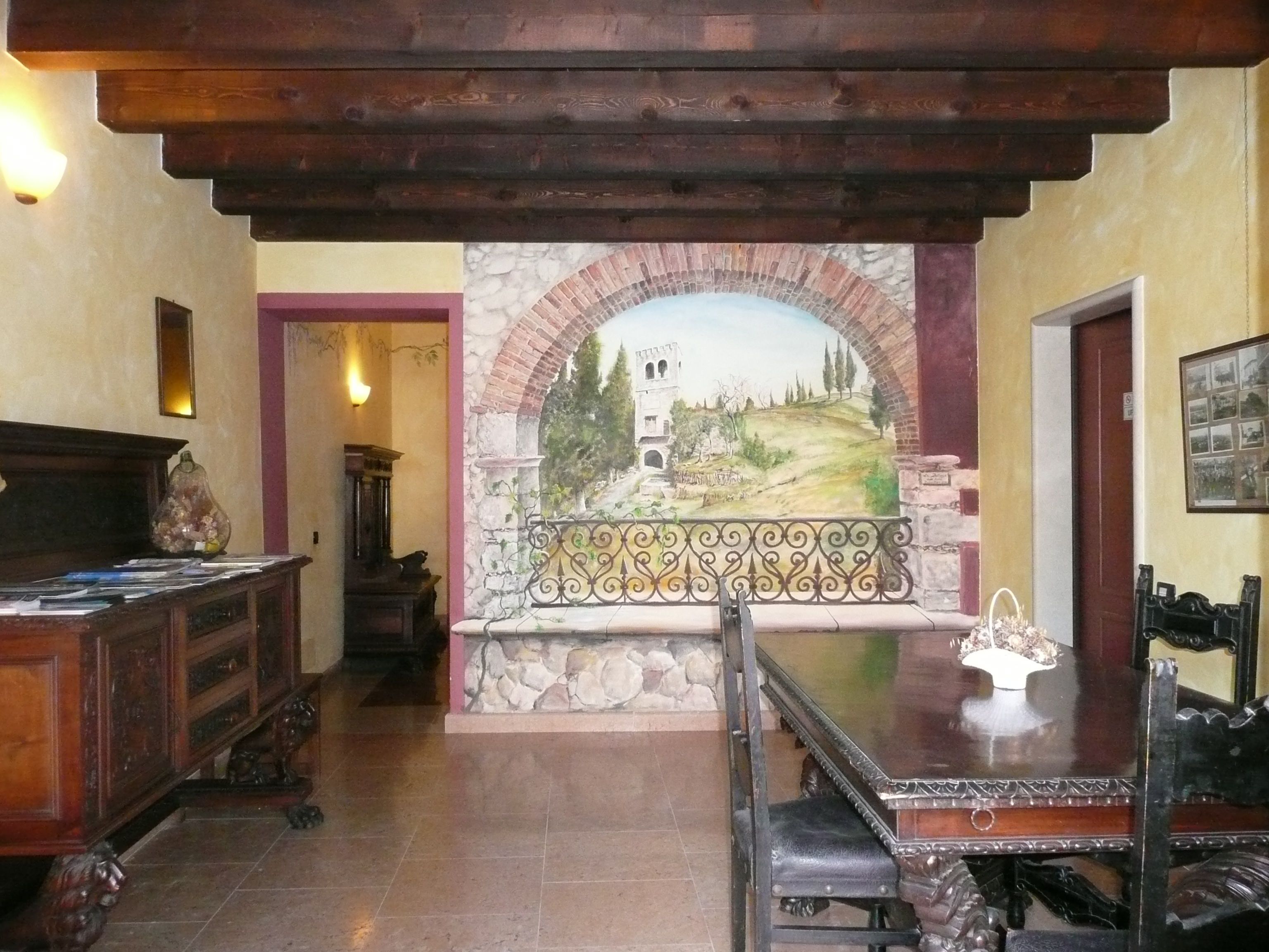 Una habitación con un arco de piedra que conduce a un mural, un escritorio de madera y un banco.