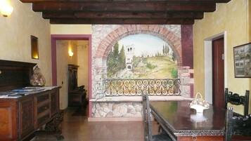 Una habitación con un arco de piedra que conduce a un mural, un escritorio de madera y un banco.