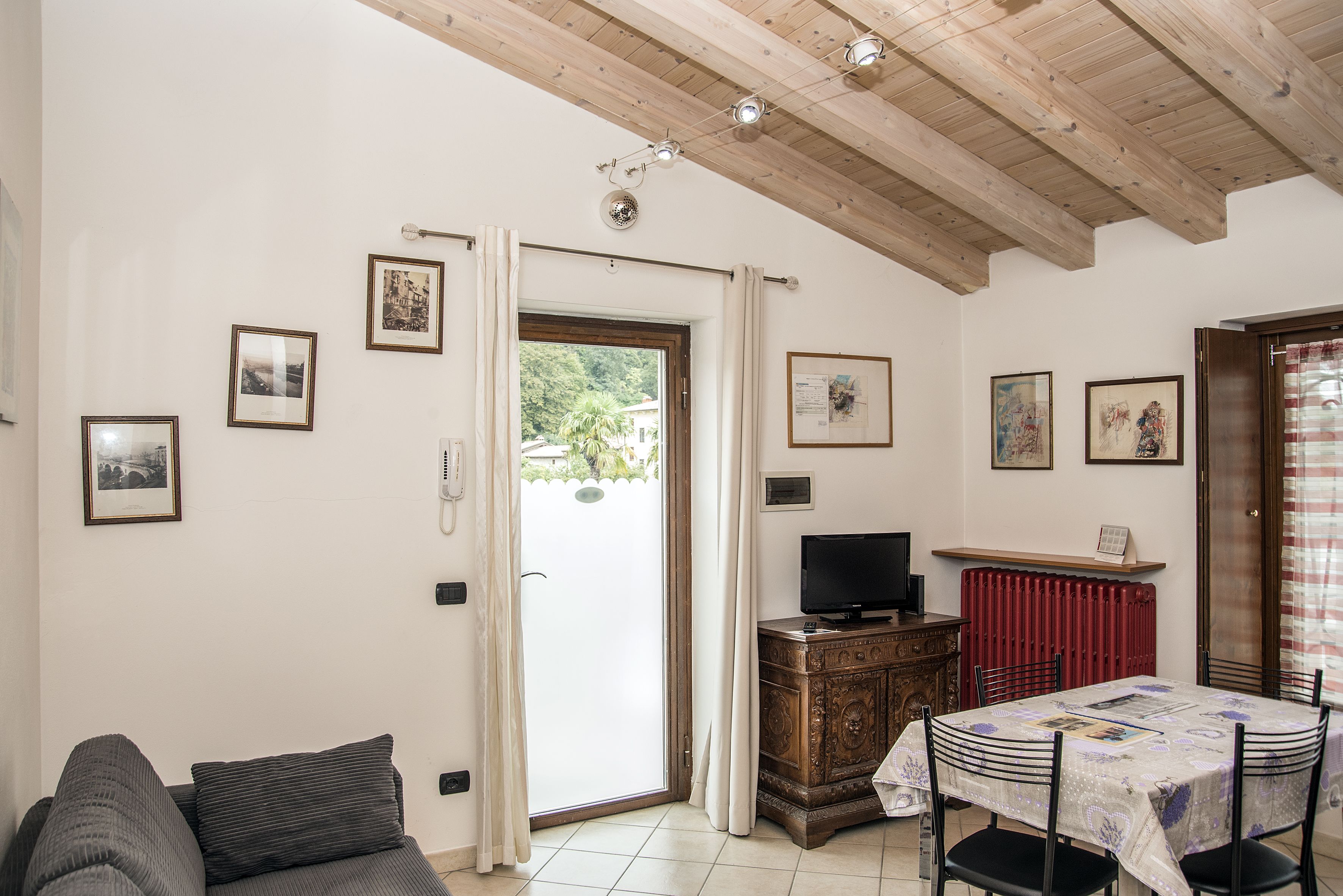 Een woonkamer met een bank, een televisie op een houten kast, een eettafel met stoelen en een deur naar een balkon.