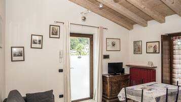 Een woonkamer met een bank, een televisie op een houten kast, een eettafel met stoelen en een deur naar een balkon.