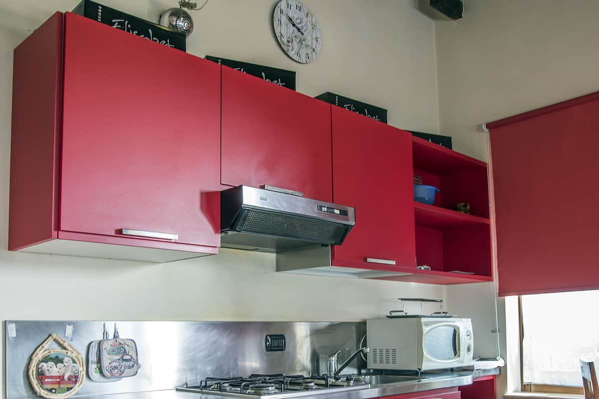 A kitchen with red cabinets, a microwave, and a clock on the wall.